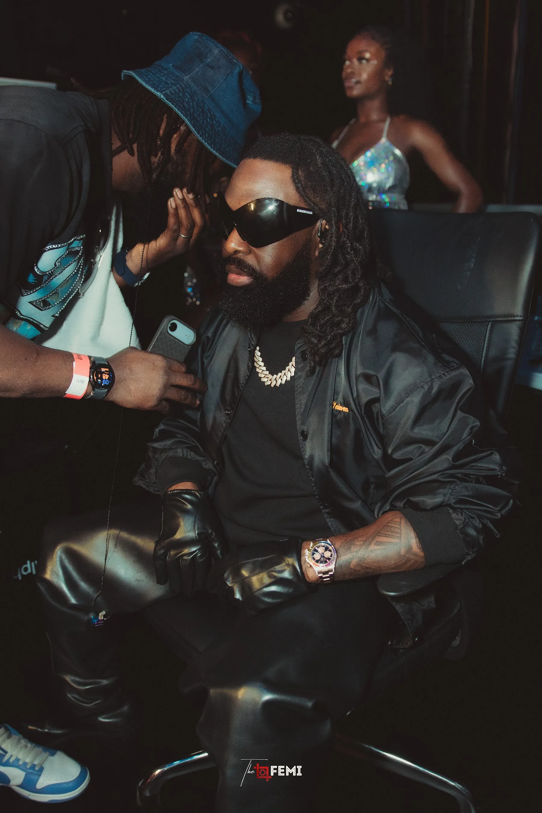 Portrait of Timaya seated backstage in a black jacket